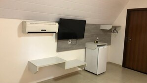 A compact kitchenette with a built-in refrigerator, a wall-mounted TV, and a small shelf unit. - HOTEL RECANTO DO BOSQUE (Sorriso)