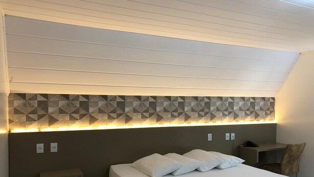 A hotel room with a bed, bedside table, and a headboard with geometric patterned tiles. - HOTEL RECANTO DO BOSQUE (Sorriso)