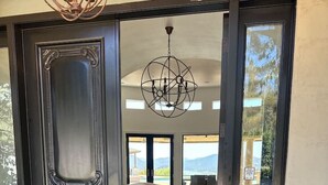 A grand entrance with a dark wooden door, a modern chandelier, and a view of a spacious living area with a white sofa and a pool. - Private Gated 6BR Luxury Estate, Gym, Lake View (Escondido)