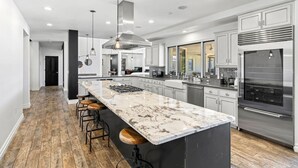 A modern kitchen with a large island, stainless steel appliances, and a wooden floor.