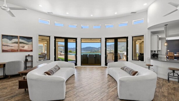 A spacious living room with a curved ceiling, large windows, and a view of a pool and mountains.
