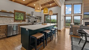 Una cocina amplia con una isla grande, techo de madera y ventanas grandes que ofrecen vistas al exterior.
