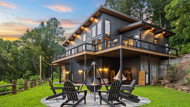 Una casa moderna de dos pisos con un porche cubierto, mobiliario exterior y una chimenea.