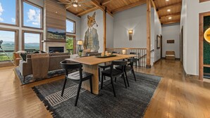 Amplia sala de estar con techo de madera, chimenea, mesa de comedor con sillas y un gran ventanal con vistas al exterior.