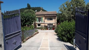 A gated entrance leading to a two-story building with a tiled roof, surrounded by greenery and a clear sky. - Maison provençale Coeur du Var (first floor) (GONFARON)