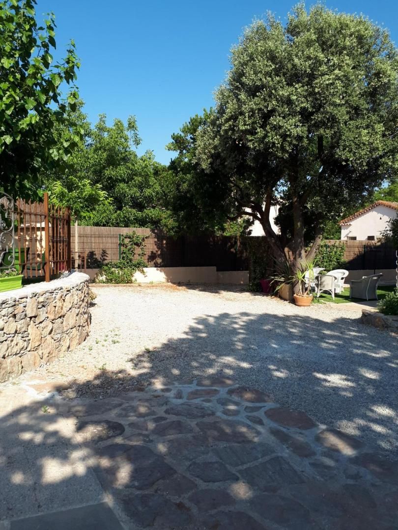 Un patio con piso de piedra, un portón de madera y un gran árbol que da sombra.