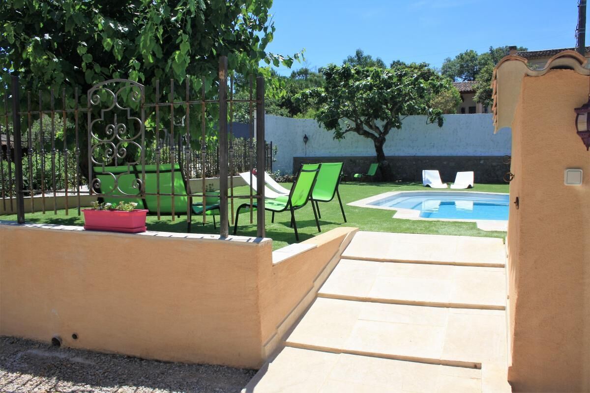 A backyard with a pool, green chairs, and a fenced area with a decorative gate.