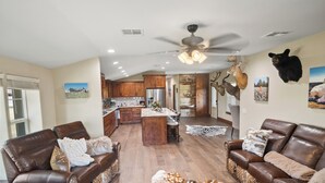 A spacious living room with leather sofas, a large rug, and a ceiling fan. - Refuge Hunting Cabin (Elgin)