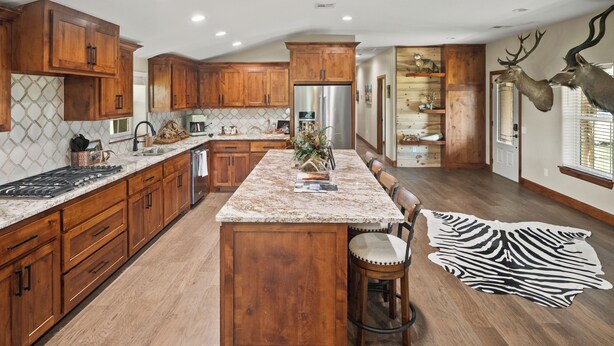 A spacious kitchen with wooden cabinets, a large island, and a zebra rug. - Refuge Hunting Cabin (Elgin)