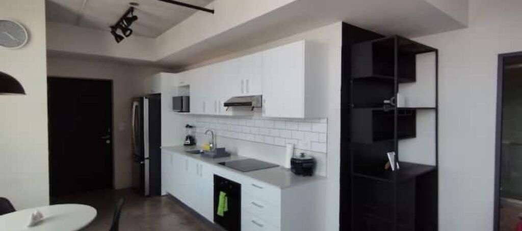 A modern kitchen with white cabinets, a black countertop, and a black shelving unit.