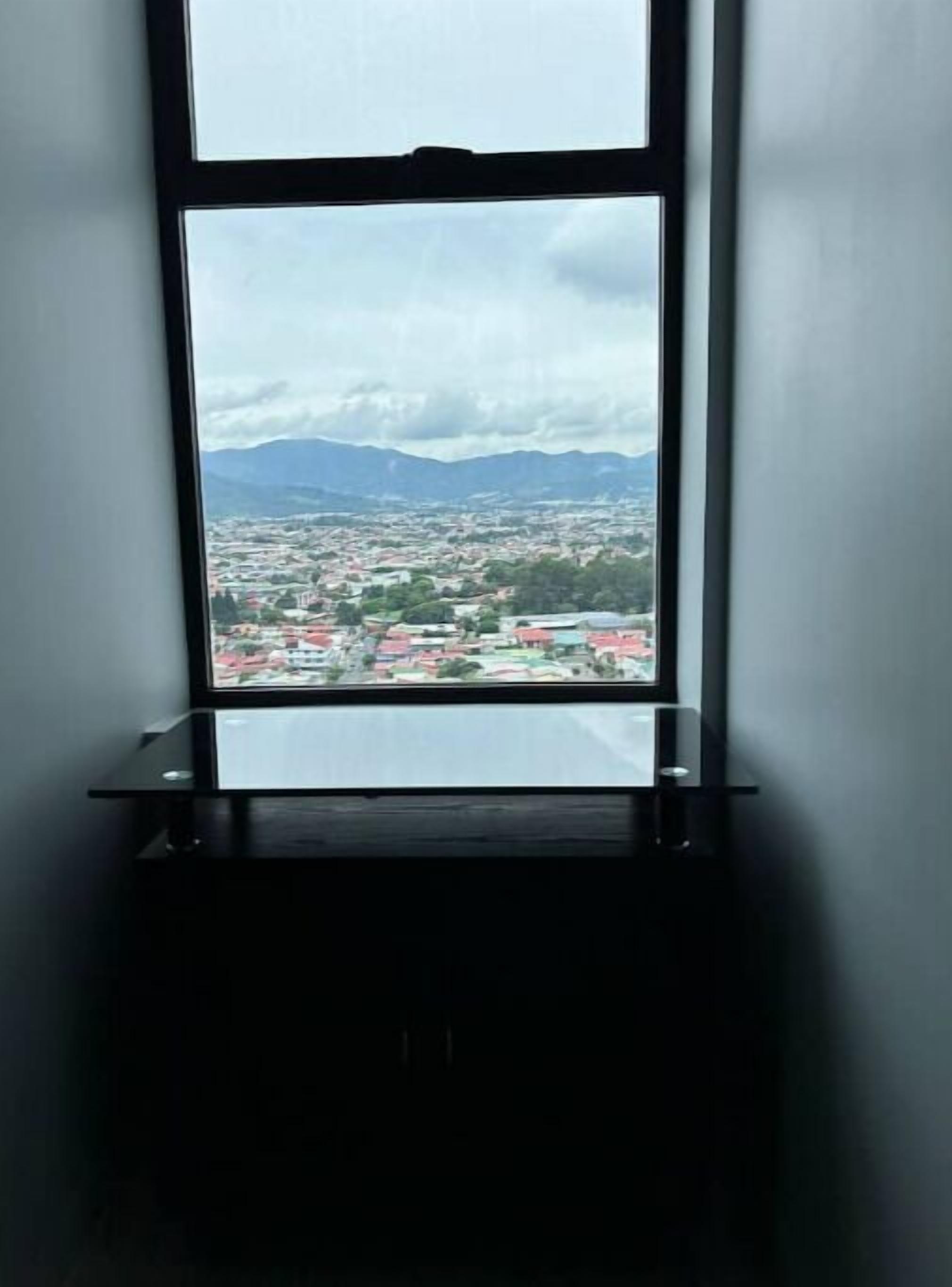 Una ventana con vistas a un paisaje urbano y montañas.