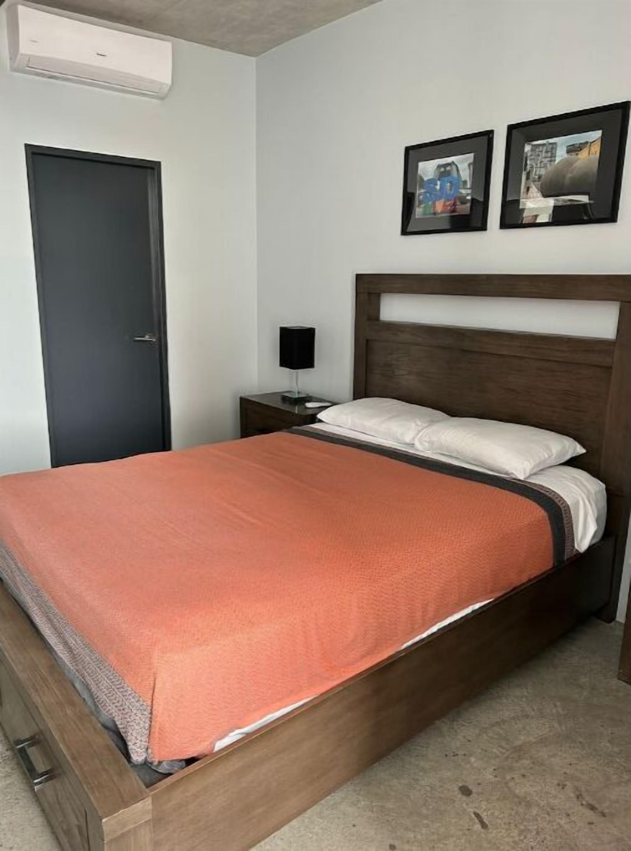 Een slaapkamer met een houten bed, een nachtkastje met een lamp, een deur en twee ingelijste foto's aan de muur.