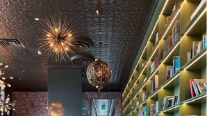 A modern library with a long wooden table and chairs, surrounded by tall bookshelves filled with books. - URBN Getaway (San Jose)