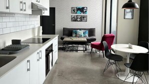 A modern kitchen with white cabinets, a black countertop, and a dining area with a round table and black chairs. There is a sofa with colorful cushions and a red chair in the background. - URBN Getaway (San Jose)