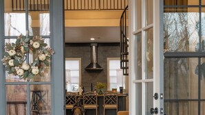 Una porta aperta che dà su una sala da pranzo con un tavolo di legno apparecchiato per due persone, un cane visibile attraverso la porta e una ghirlanda decorativa al muro.