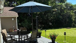 Una terraza de madera con una mesa, sillas, un paraguas y plantas en macetas.