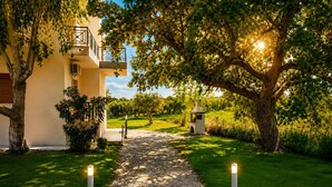A pathway leading to a building with a balcony, surrounded by trees and a well-maintained lawn. - Charming 1 triple-bedroom  in quaint Georgioupoli with AC (Georgioupoli)