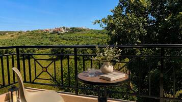 A balcony with a table, chair, and potted plant, overlooking a green landscape and buildings.