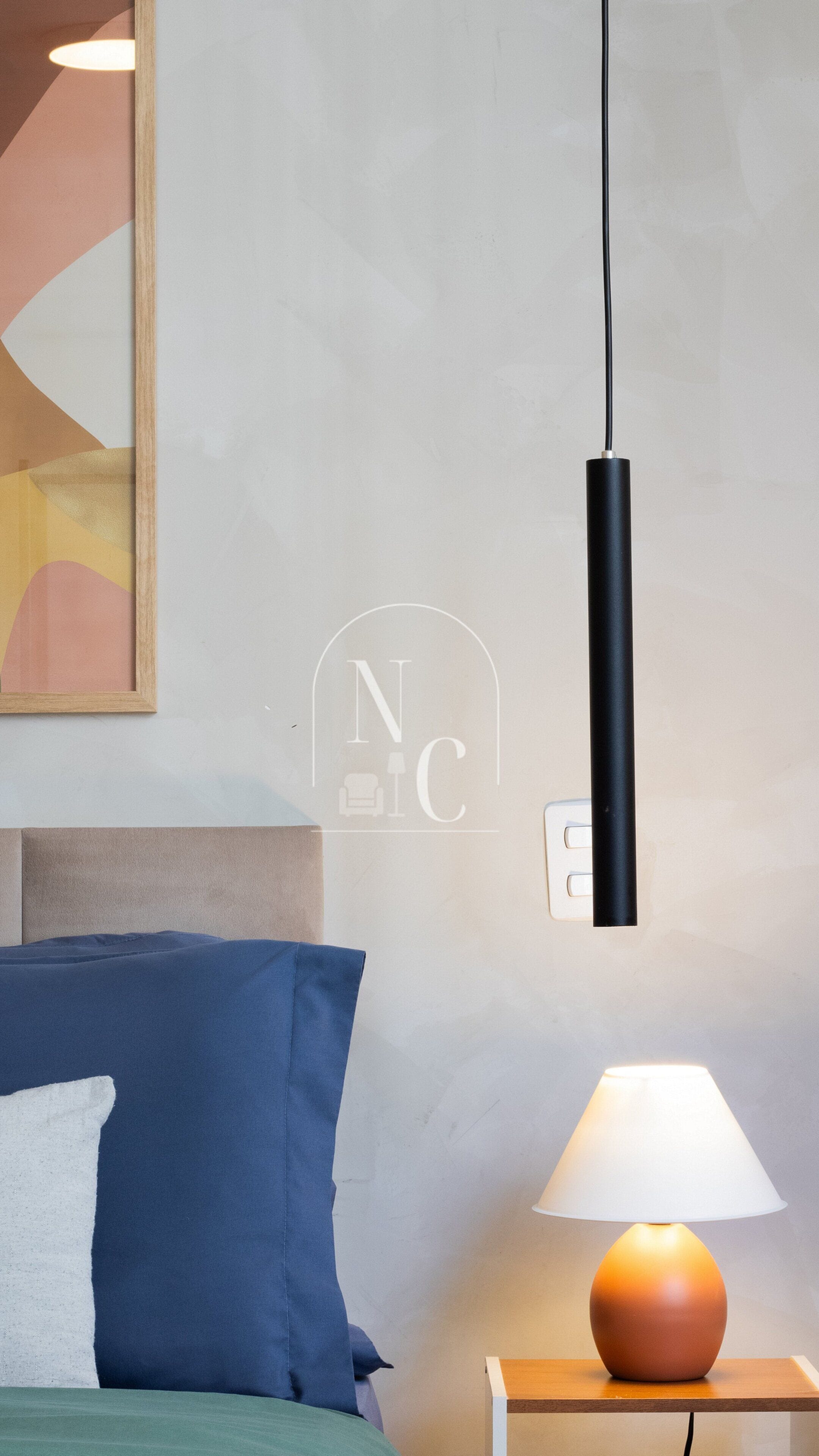 Une chambre à coucher avec un lit, des oreillers, une table de chevet avec une lampe et un luminaire fixé au mur.