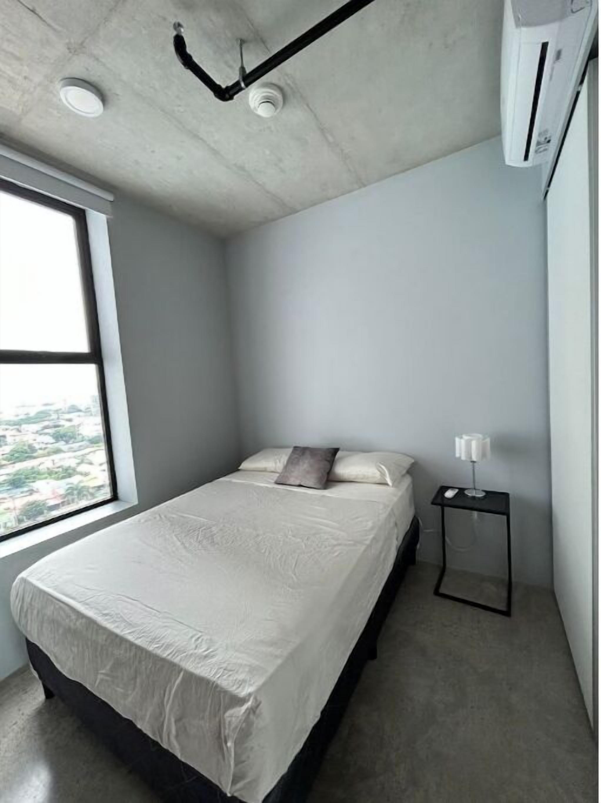 Un dormitorio pequeño y moderno con una cama individual, una mesita de noche y una ventana que ofrece vistas de la ciudad.