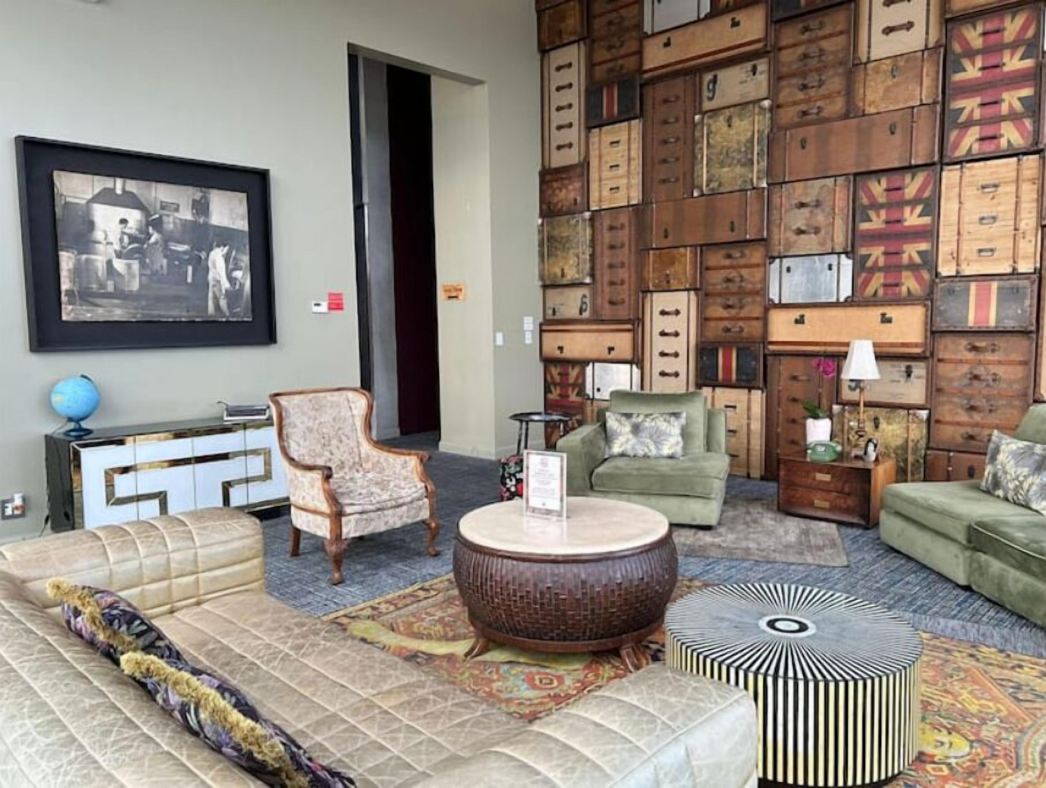 Un salon comprenant un canapé, des fauteuils, une table basse et un mur où sont empilées des valises.