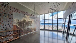 A spacious room with a large mural of palm trees and a cityscape, modern pendant lights, and a view of the city through large windows.