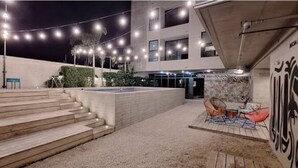 A modern outdoor area with steps leading to a seating area, a pool, and a building with a unique facade.