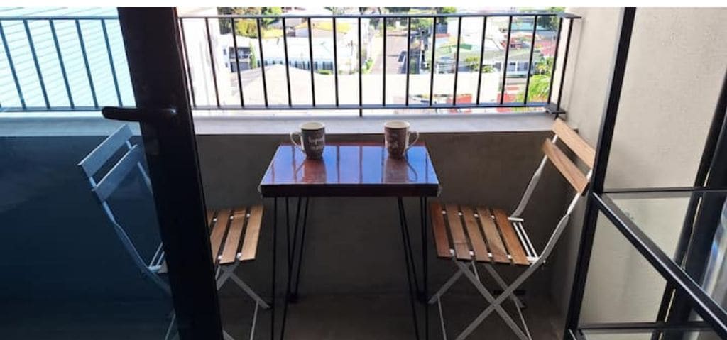 A balcony with a table and two chairs, a railing, and a view of the street.