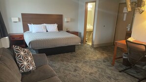 A hotel room with a bed, a desk, a chair, and a sofa. - Lincoln Hotel - King Deluxe (Lincoln)