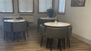 Una habitación con cuatro mesas redondas, cada una con sillas, y ventanas amplias con persianas.