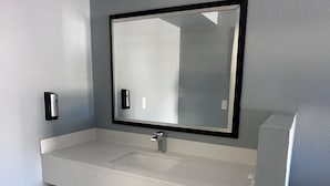 A bathroom with a white speckled countertop, a rectangular mirror with a black frame, and a wall-mounted soap dispenser. - Airport Motor Inn (Jacksonville)