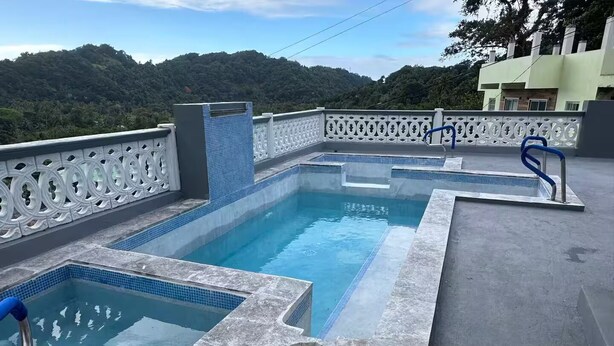 A rooftop swimming pool with a view of a forested hill. - H'Eden Treasures Studio 2 (Belle Plaine)