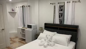 A hotel room with a bed, a bedside table, a microwave, and a shower area. - H'Eden Treasures Studio 2 (Belle Plaine)