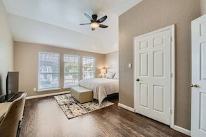 Um quarto com cama, escrivaninha, ventilador de teto e porta.