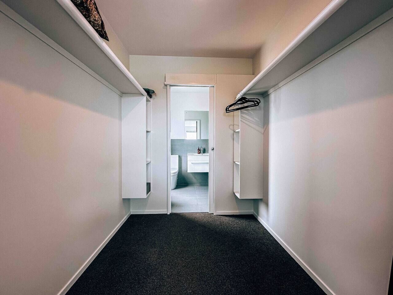 A narrow hallway with a carpeted floor leading to a bathroom with a toilet and sink.