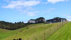 A modern house on a grassy hill with a fenced pasture below.