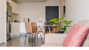 A modern living room with a sofa, a dining table with chairs, and a kitchen area in the background. - Lovely 1 bedroom unit - fully equipped - 100mbps (San Jose)