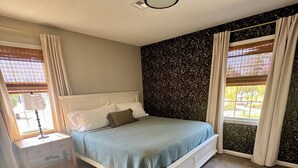 Ein Schlafzimmer mit Bett, Nachttisch und Fenster mit Vorhängen.