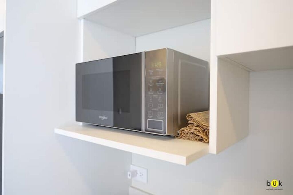 A modern kitchen with a built-in microwave on a white shelf.