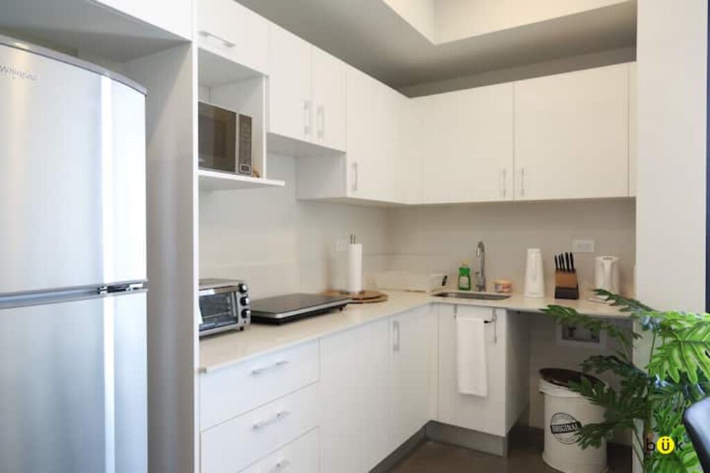 A modern kitchen with white cabinets, a built-in oven, a toaster, and a sink.