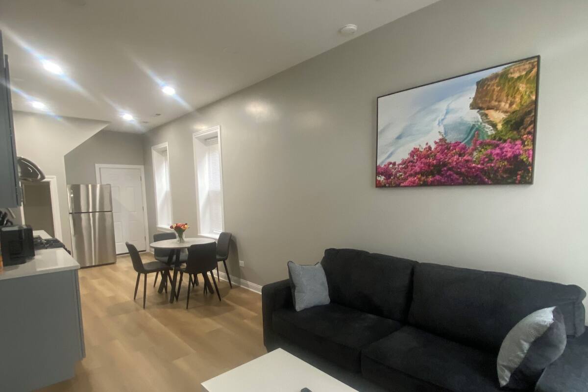 Ein modernes Wohnzimmer mit einem dunklen Sofa, einem weißen Couchtisch und einem Gemälde einer Küstenlandschaft.