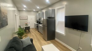 A modern living room with a black sofa, a white coffee table, and a flat-screen TV mounted on the wall.