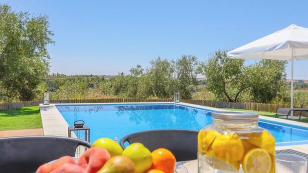 Zona junto a la piscina con vistas despejadas, rodeada de vegetación y una sombrilla blanca.