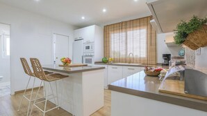 Una cocina moderna con armarios blancos, una isla central y una barra desayunadora con sillas de mimbre.