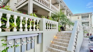 Et hotel med flere etager, hvid facade, balkon med planter og en trappe op til de øvre etager.