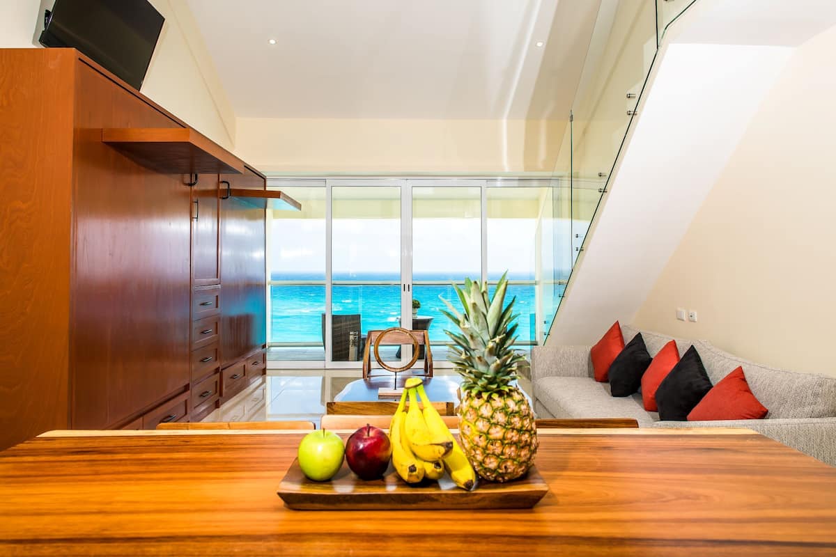 Un coin repas avec une table en bois, des fruits et une vue sur l’océan.