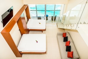A hotel room with two beds, a sofa with red cushions, a TV, and a balcony with a view of the sea. - Salvia (Cancún)