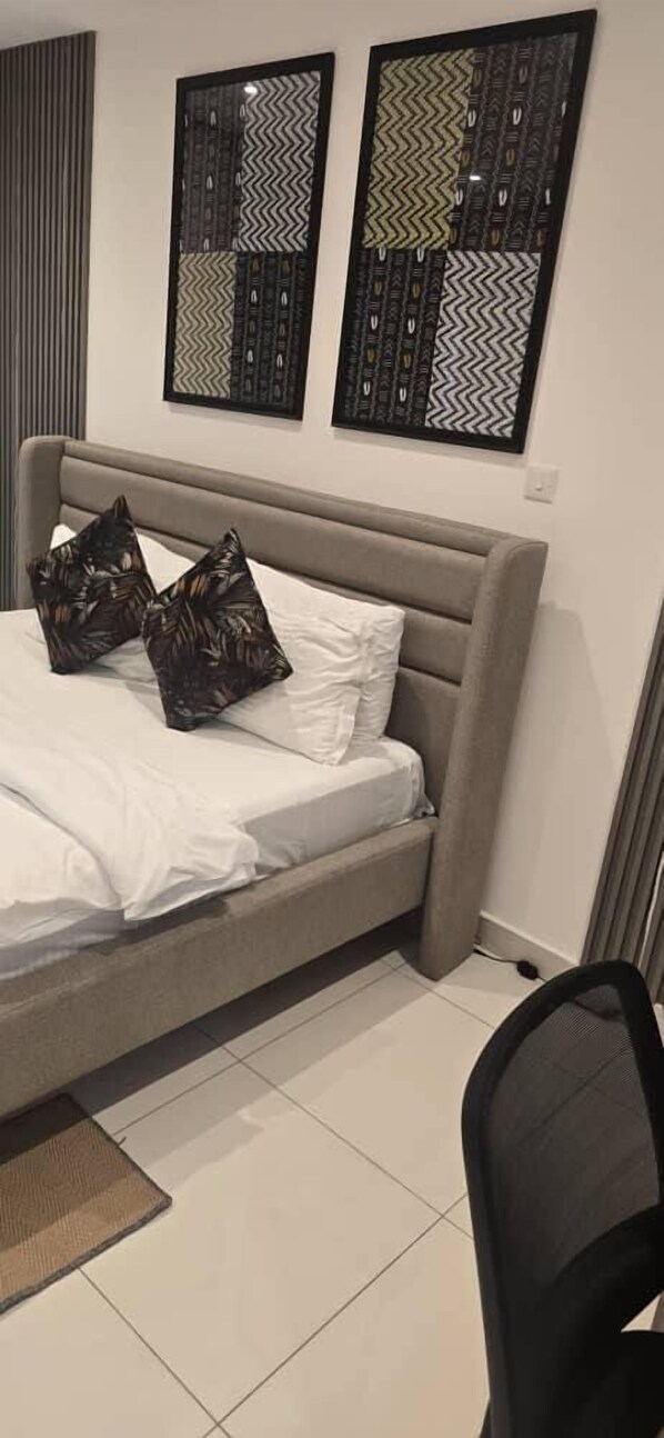 A bedroom with a bed, two pillows, a chair, and two framed wall art pieces.