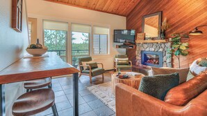 Un salon chaleureux avec un plafond en bois, une cheminée, un téléviseur et des fauteuils confortables.