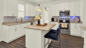 A modern kitchen with white cabinetry, granite countertops, stainless steel appliances, and a central island with bar stools.